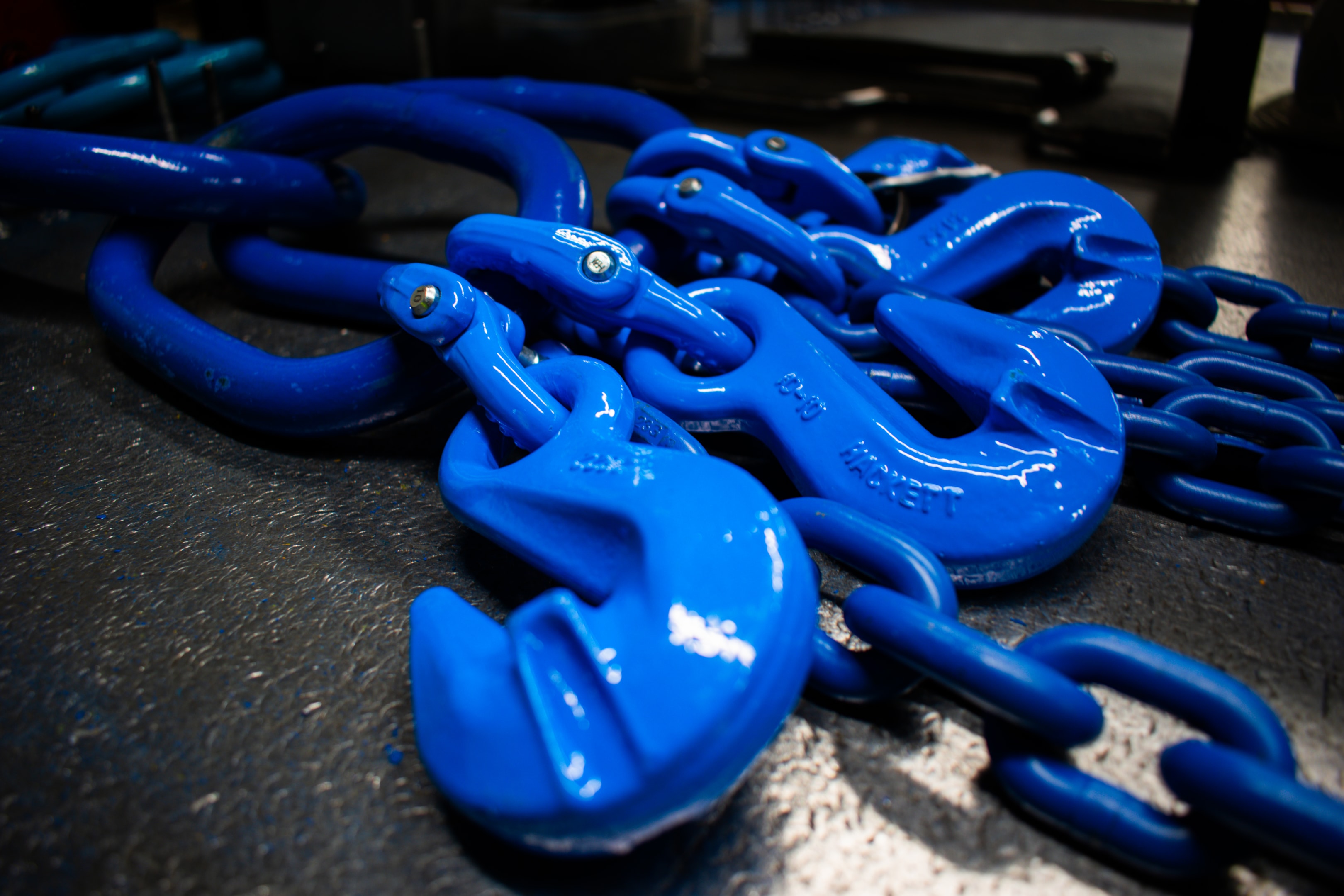 The image displays various components of chain slings, including master links, lifting chains, and different types of hooks such as self-locking and foundry hooks, all arranged neatly for easy identification. These rigging hardware parts are essential for overhead lifting applications and demonstrate the durability and versatility required for safe load handling.