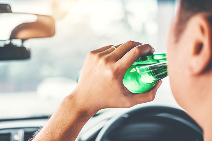 Driver drinking from a green bottle behind the wheel representing drunk driving accident liability