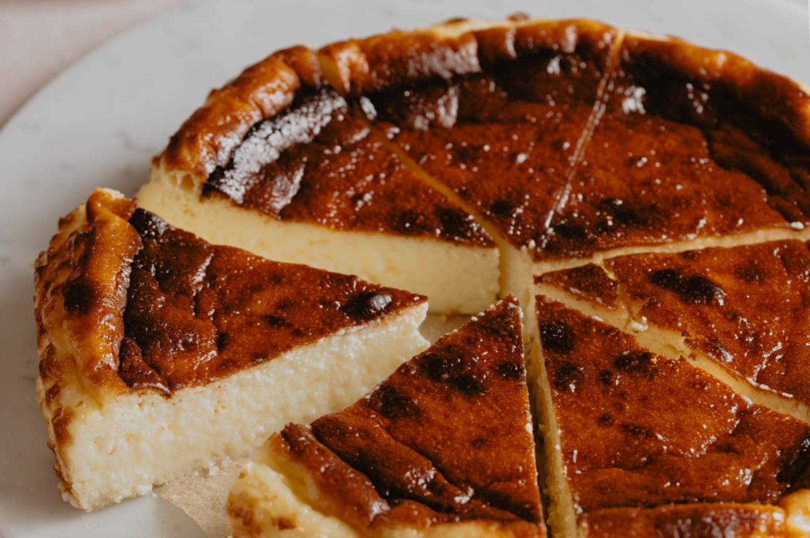 Rich, creamy cheesecake on a marble plate, with a golden, caramelized top. One slice slightly removed, revealing its smooth, velvety interior.