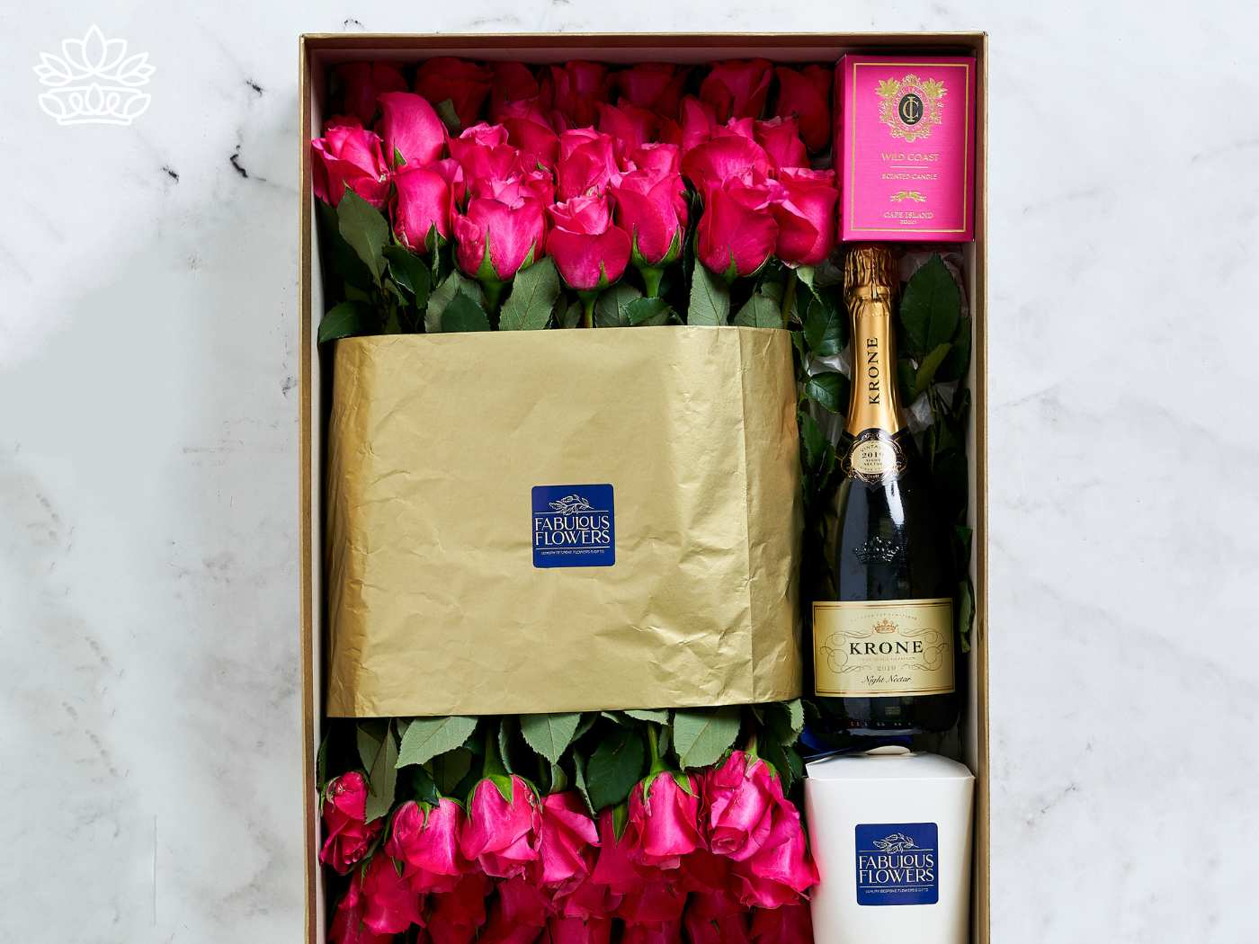 Luxurious graduation gift from Fabulous Flowers and Gifts featuring a bouquet of vibrant pink roses, a bottle of Krone sparkling wine, and a Wild Coast fragrance candle, thoughtfully packaged and ready to be delivered with heart