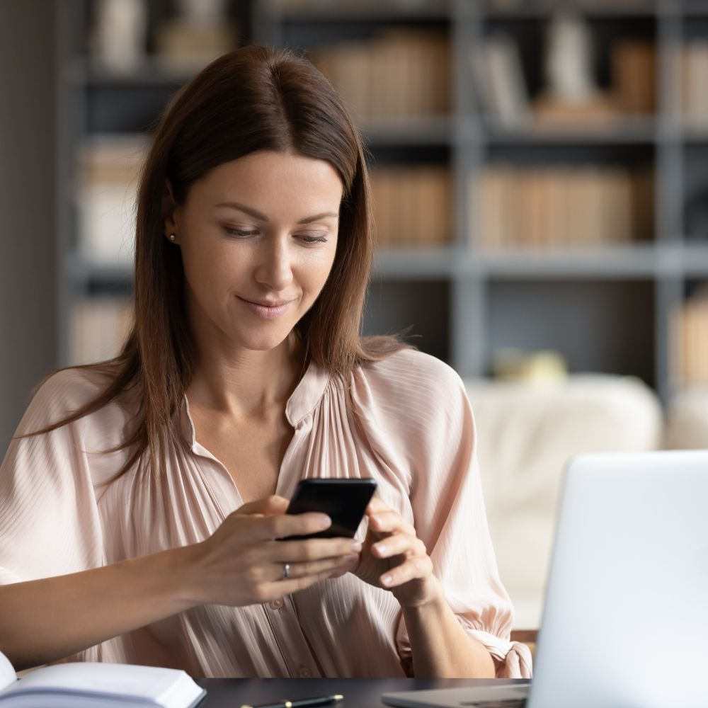 A person using a laptop and looking at a phone while smiling