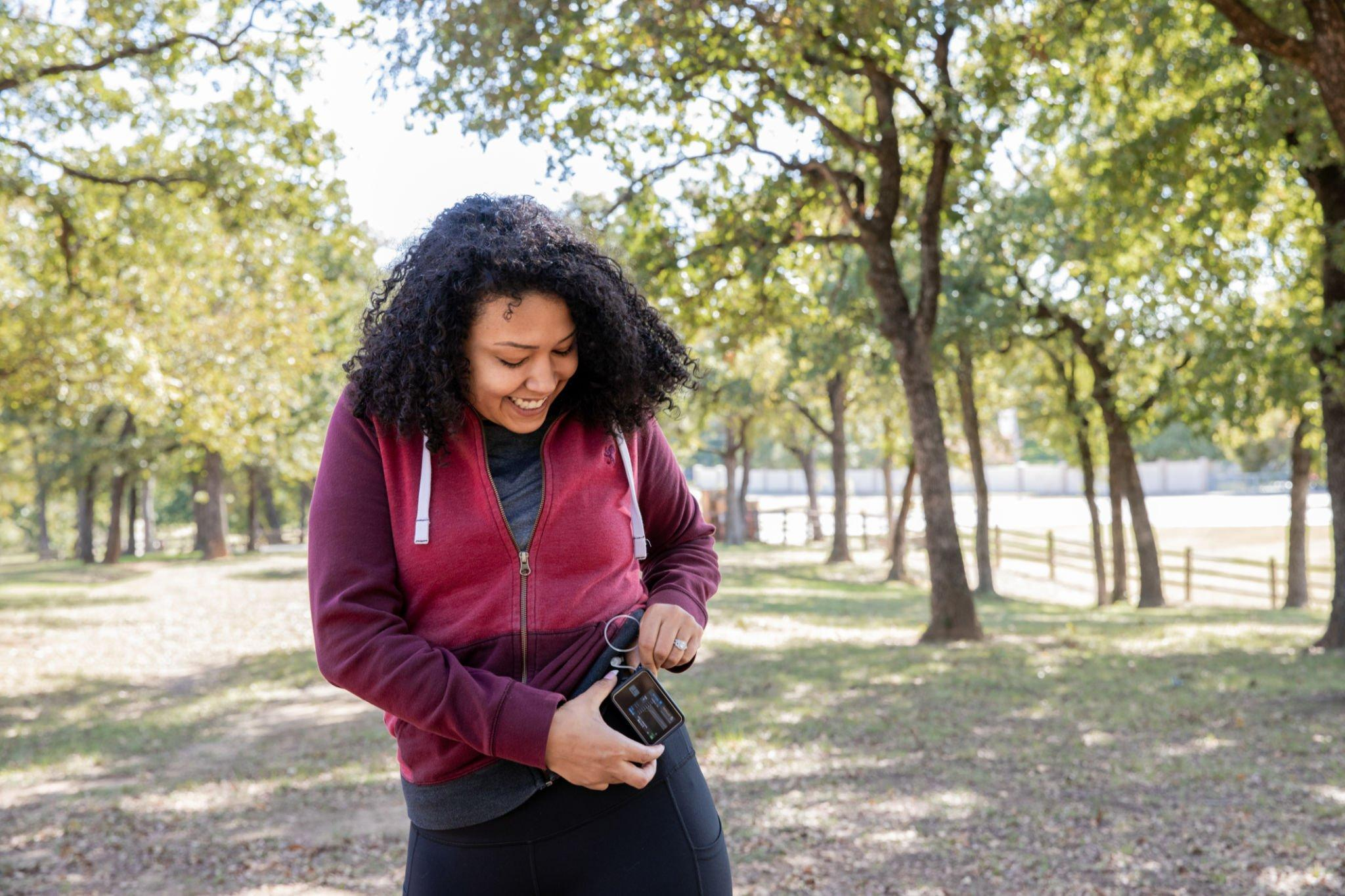 Image of a happy woman checking her CGM device monitor through the Freestyle LibreLink app on certain mobile devices, accessing valuable sensor glucose information