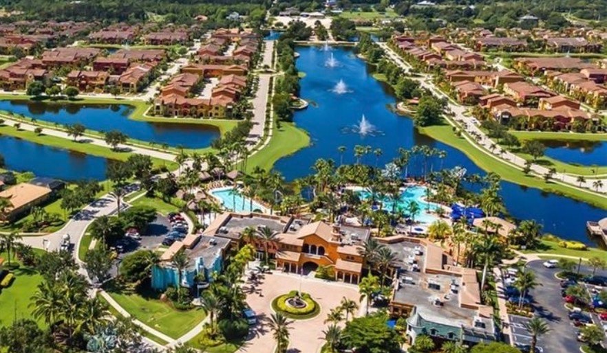 An aerial view showcases the prestigious Paseo gated community in Fort Myers, featuring beautifully designed Mediterranean-style homes surrounded by lush landscaped grounds and expansive park views. The image highlights the resort-style living and incredible amenities that make this award-winning community a desirable place to call home.