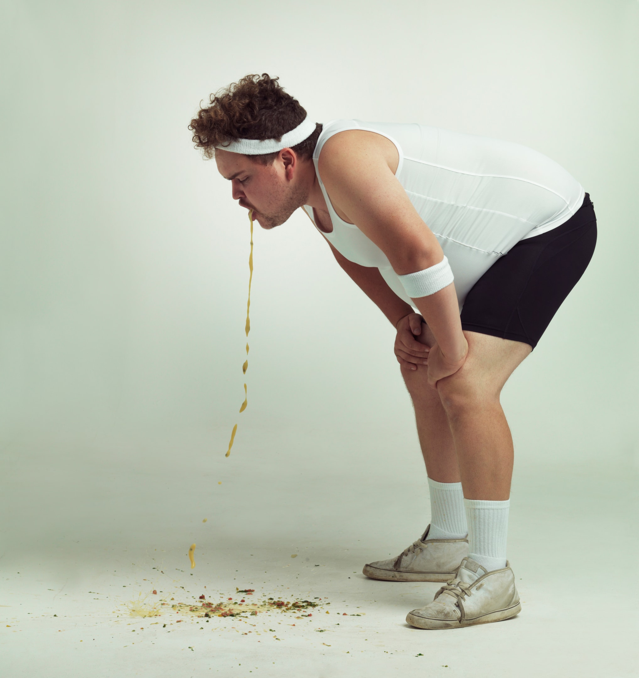 A man in athletic wear bent over and vomiting, depicting the severe physical distress and purging behaviors that can be a reality for those experiencing eating disorders in men.