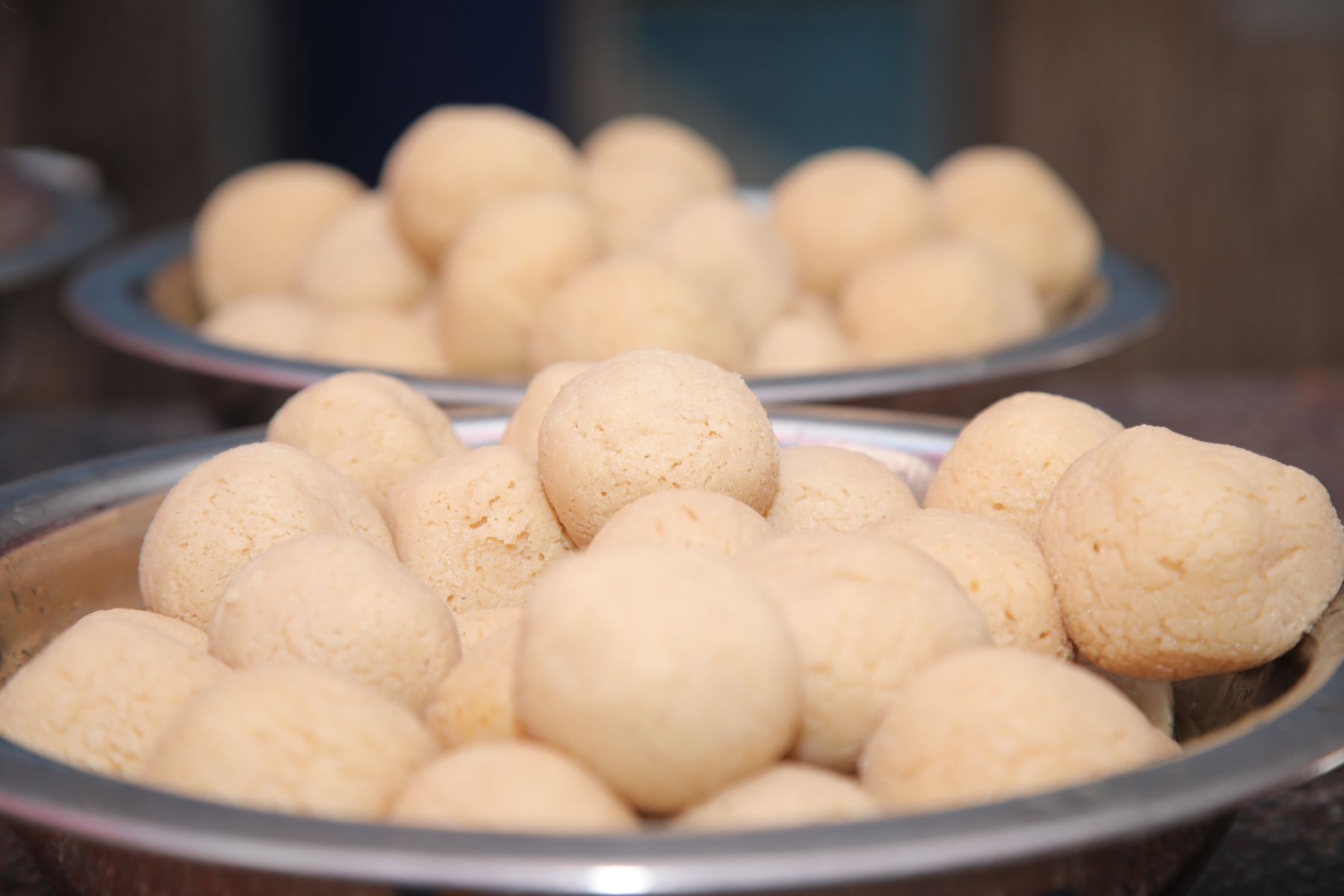 Hands forming rasgulla dough into small, round balls.