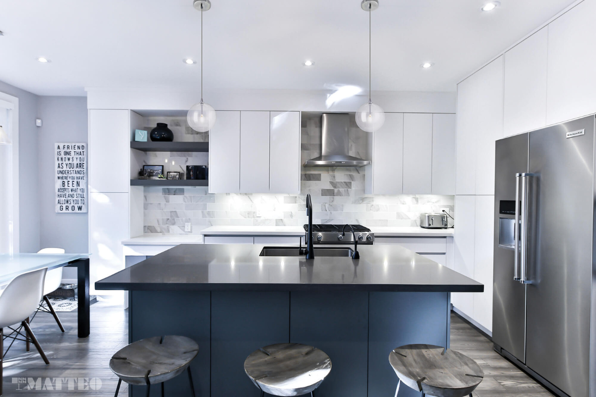 Glass pendant light fixtures over a blue kitchen island, adding modern illumination and airiness to a bright white kitchen.