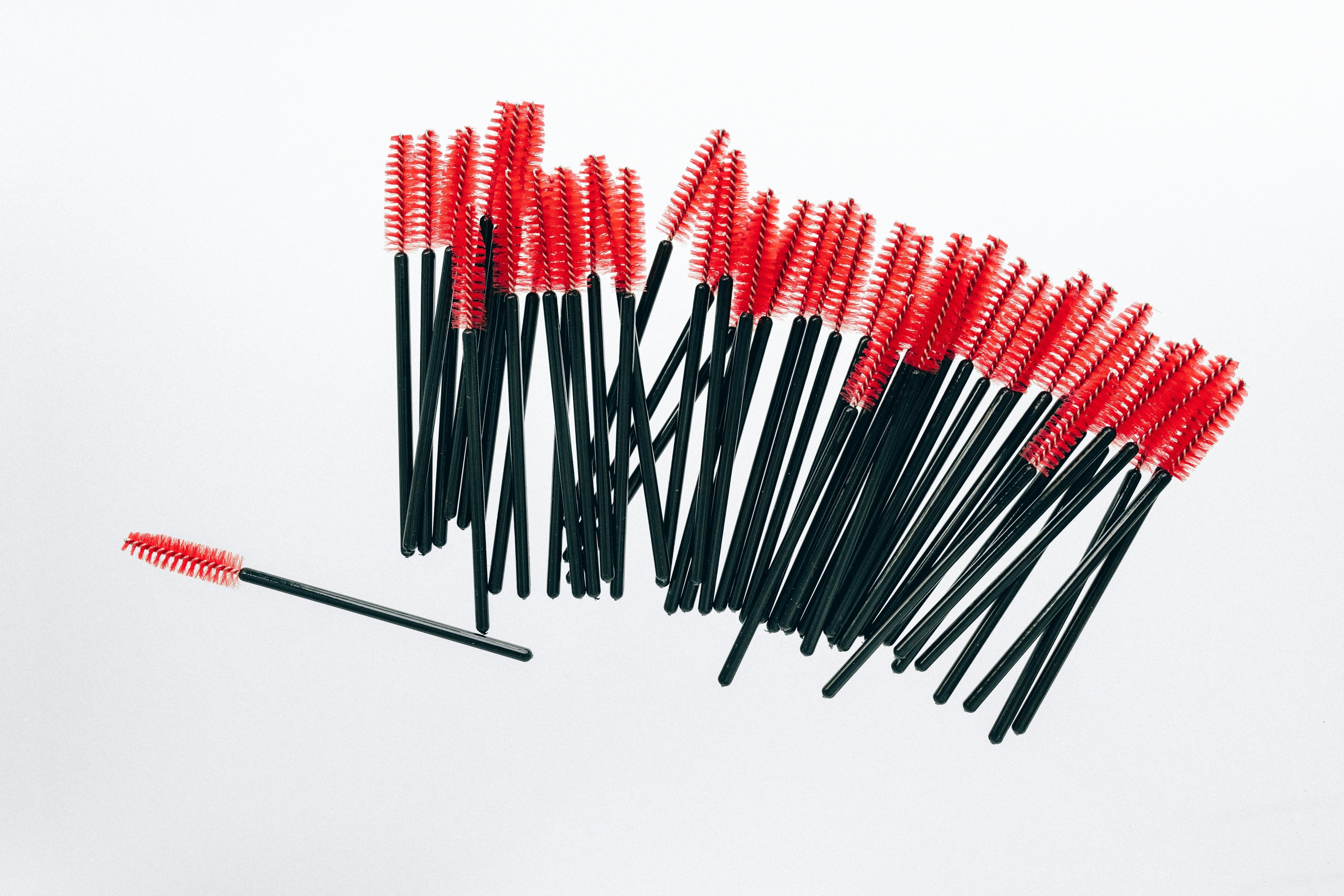 Dozens of red lash brushes laying on a table