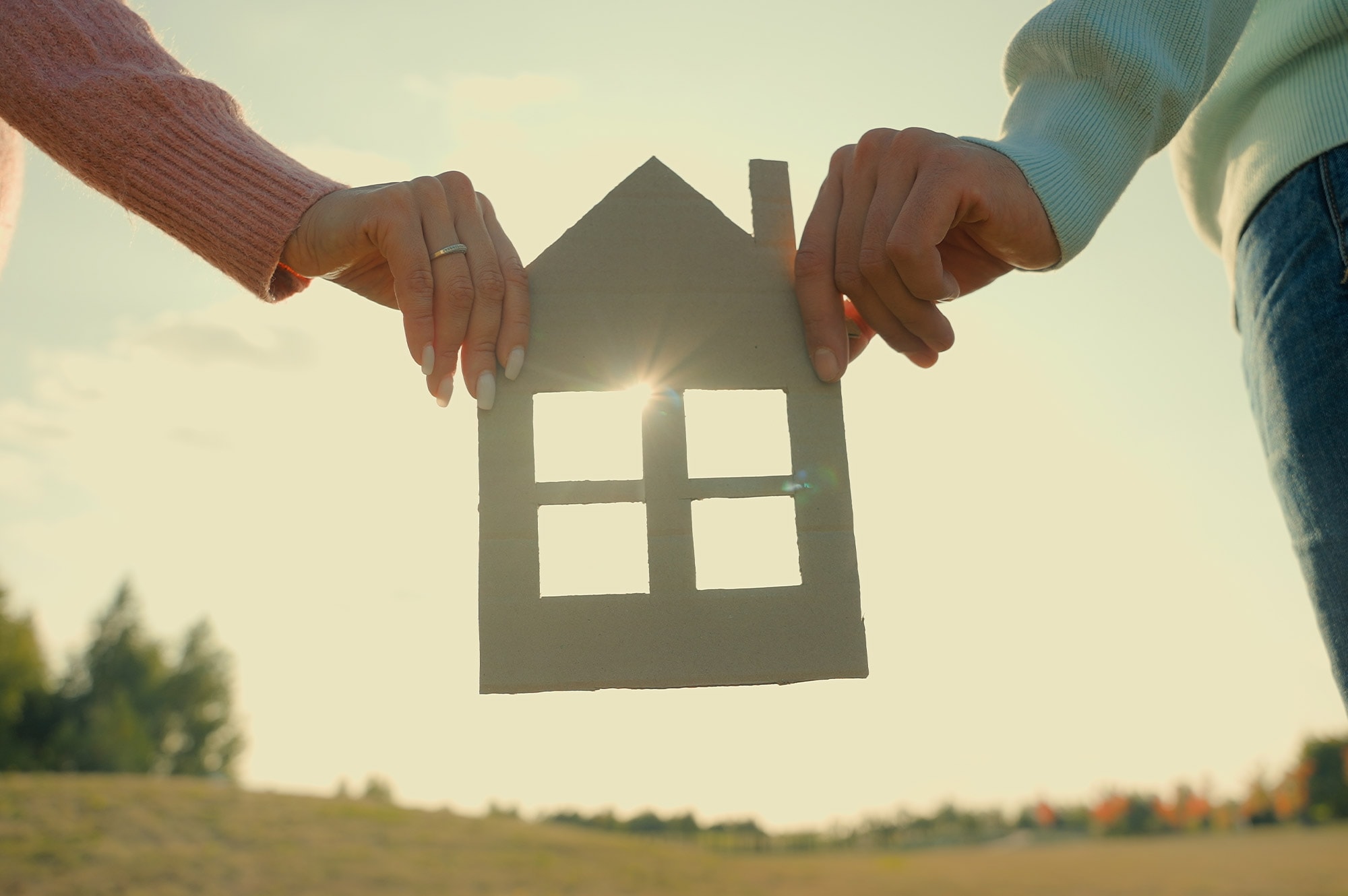 A couple holds a paper house cutout in an open field, expressing the vision of homeownership supported by Land Loans in Australia.