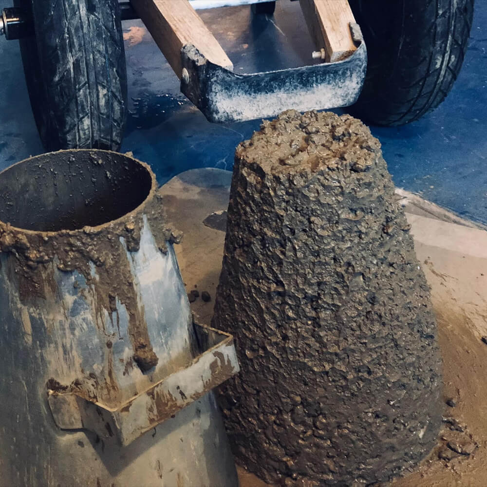 A person using a slump cone to measure the slump value of concrete mix