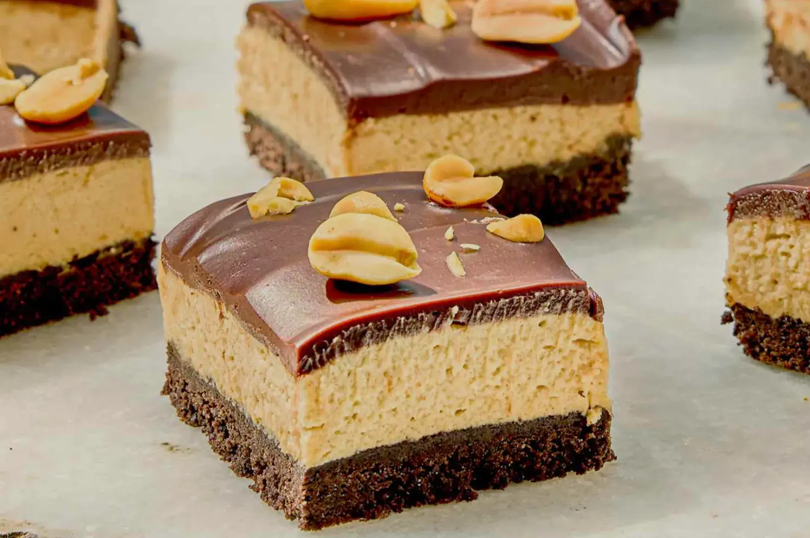 Chocolate and peanut butter dessert bars with a layer of chocolate ganache and topped with peanuts.