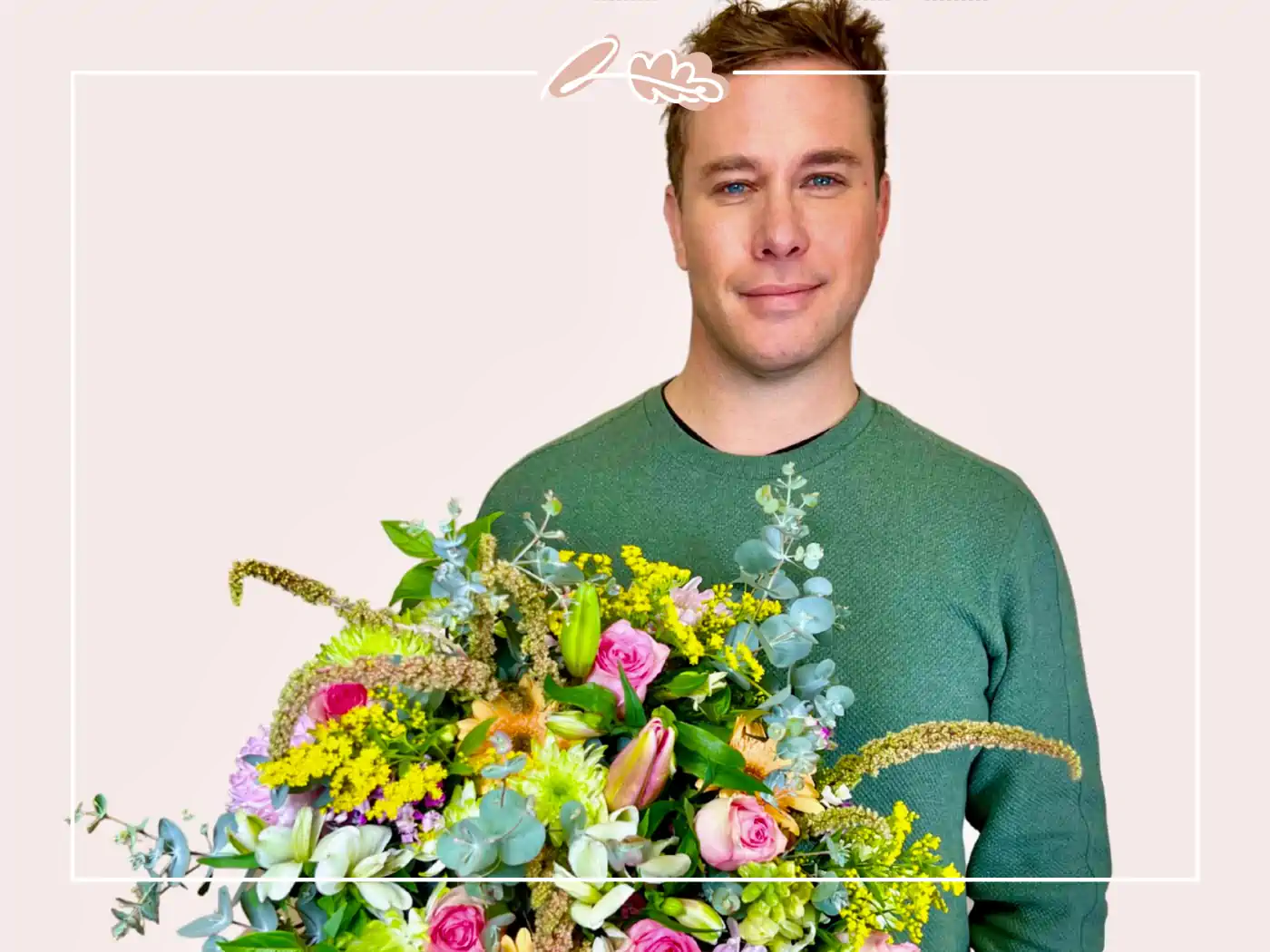 A man in a green sweater holding a colorful bouquet featuring pink roses and yellow accents, posing with a neutral expression.