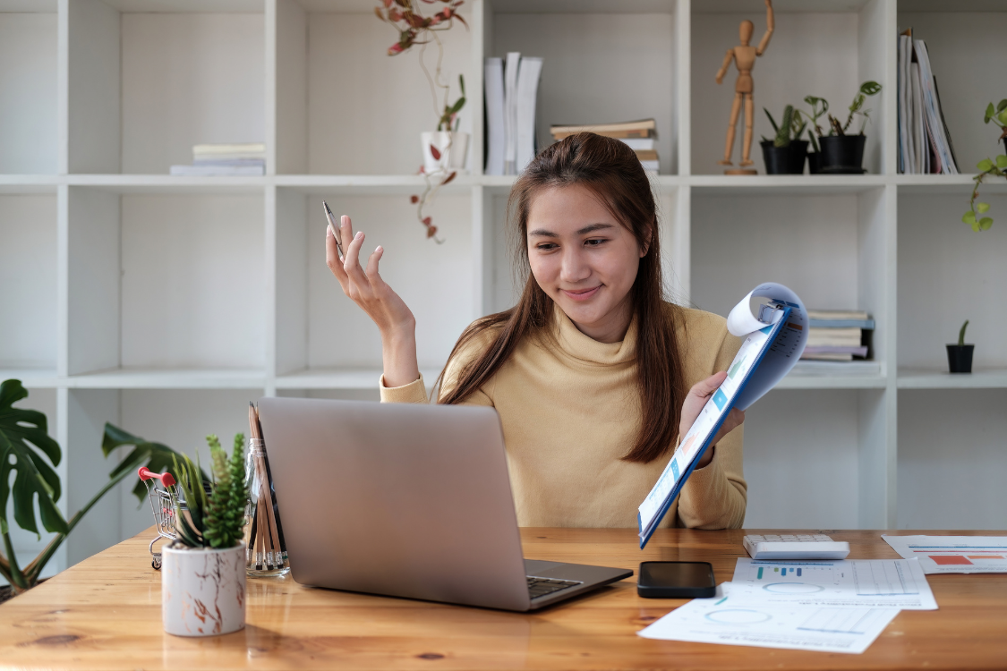 Filipina administrative assistant reviewing documents and smiling at laptop