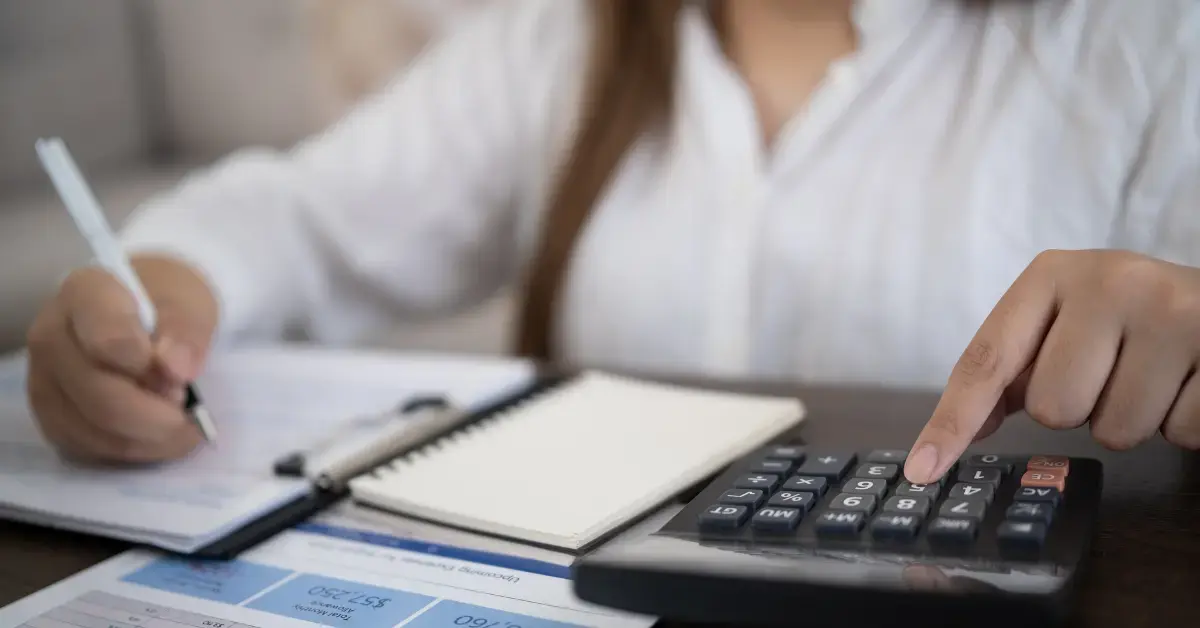 Woman reviewing IRS national standards for allowable living expenses while calculating household costs at a desk.