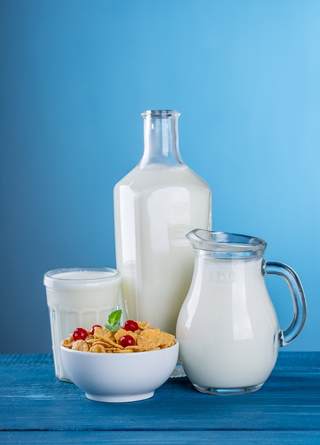 An image of a jar, pitcher, and glass of milk behind a bowl of cereal. 