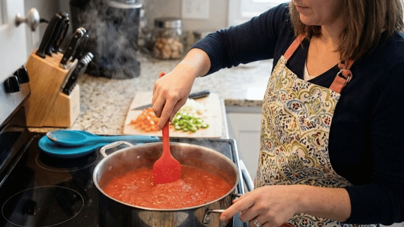 A woman is using a silicone utensil to scrape the pan.
