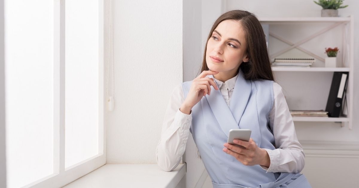 Woman contemplating taxation strategies for OnlyFans creators while holding a phone.