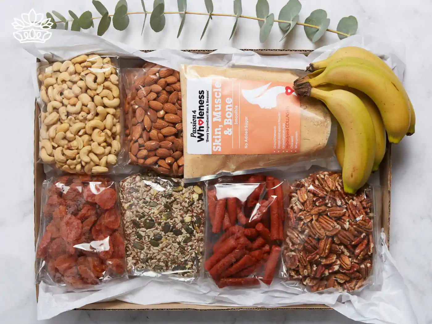 Assorted healthy snack box containing cashews, almonds, dried apricots, seed mix, saffron & honey biscuits, and fresh bananas, presented with elegant eucalyptus leaves. Guest House and Hotel Gift Boxes Delivered with Heart. Fabulous Flowers and Gifts.