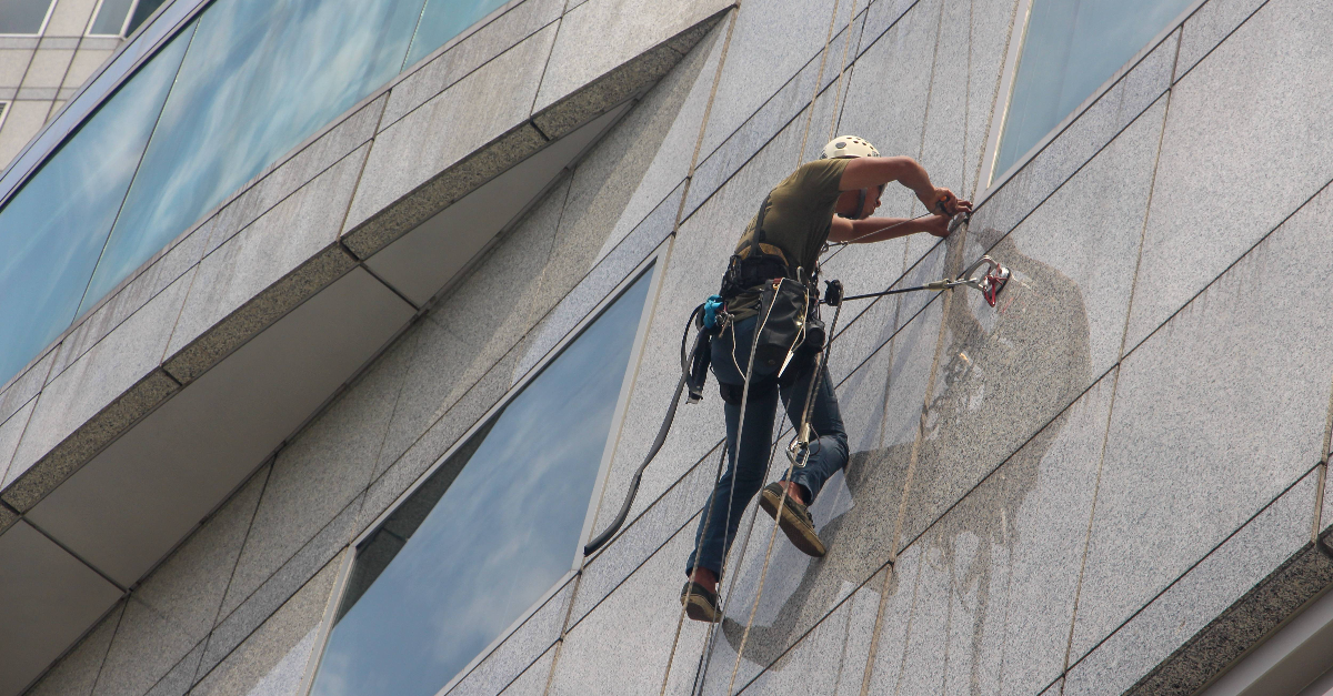 Glazenwasser aan het werk op aan de zijkant van een hoog gebouw.