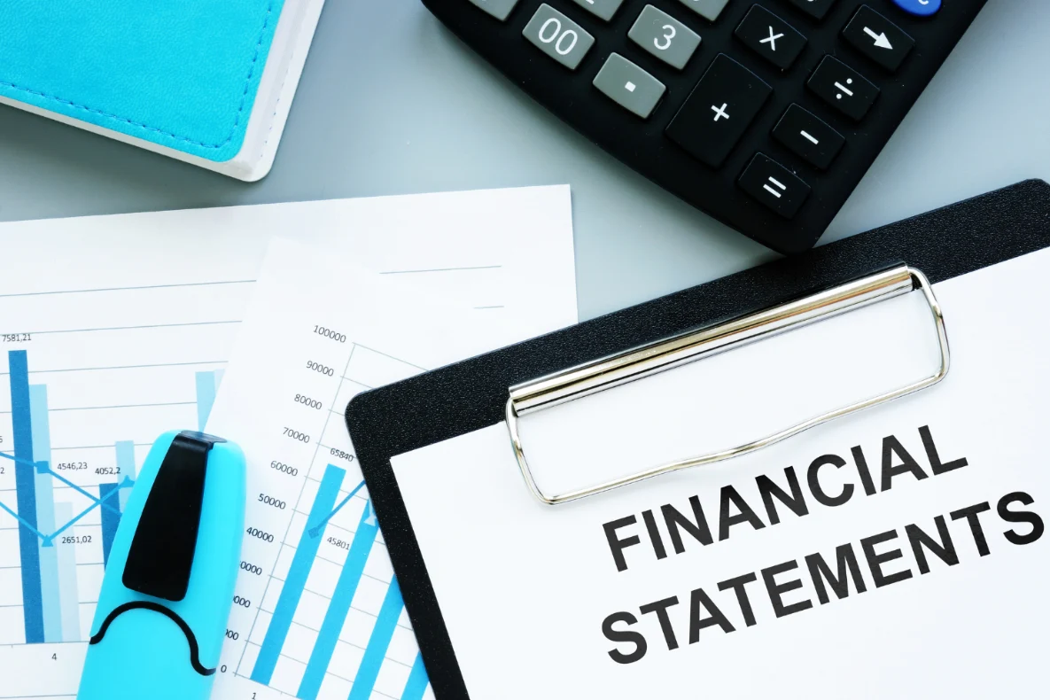 A clipboard labeled “Financial Statements” sits beside a calculator, financial charts, and a blue notebook, illustrating key tools used in business valuation small business..