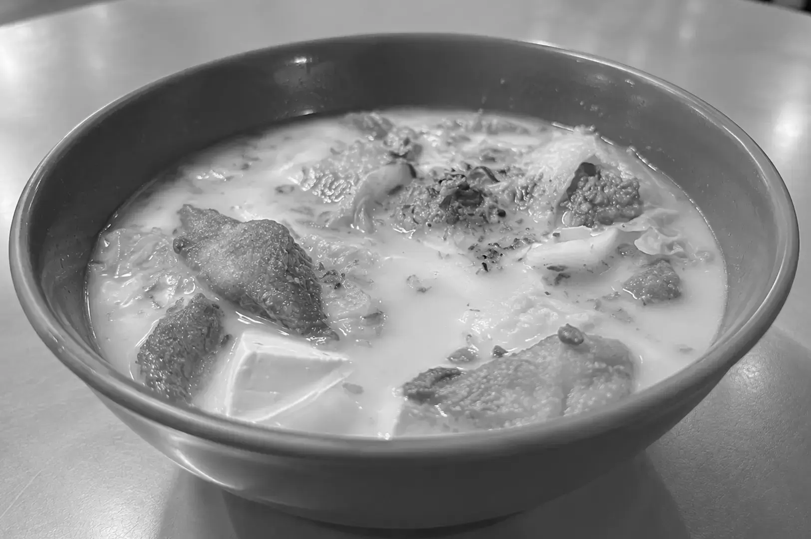 A bowl of Fish Head Bee Hoon with fried fish pieces, tofu, vegetables, and bee hoon noodles in a creamy broth.