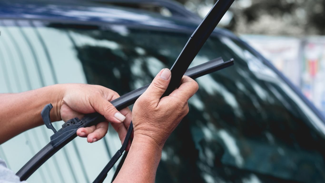 A person replacing wiper blades on a car windshield