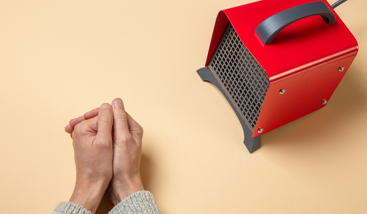 Figure warming their hands in front of a small fan heater 