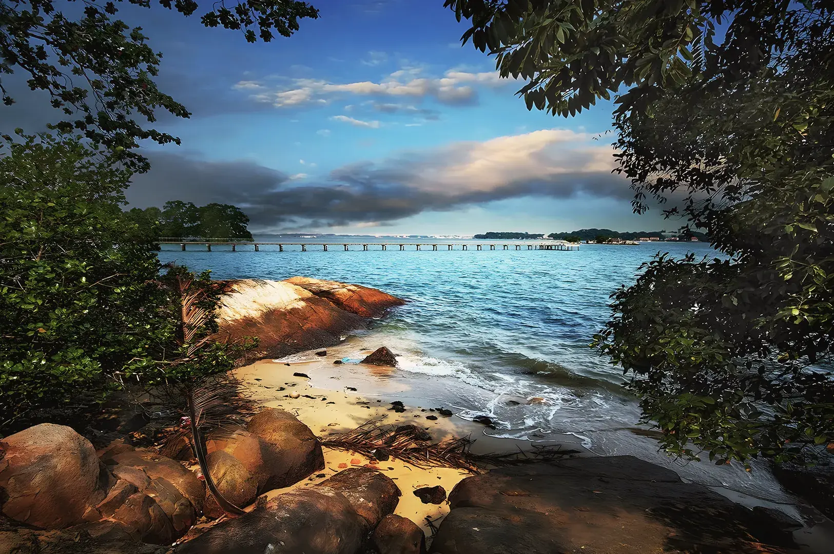 Pulau Ubin coastal landscape with rocky shore, sandy beach, and long wooden jetty stretching into calm waters