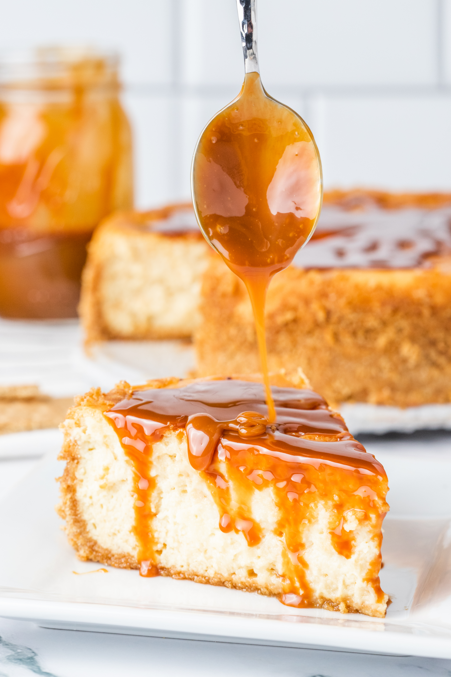 spoon drizzling caramel sauce onto slice of cheesecake