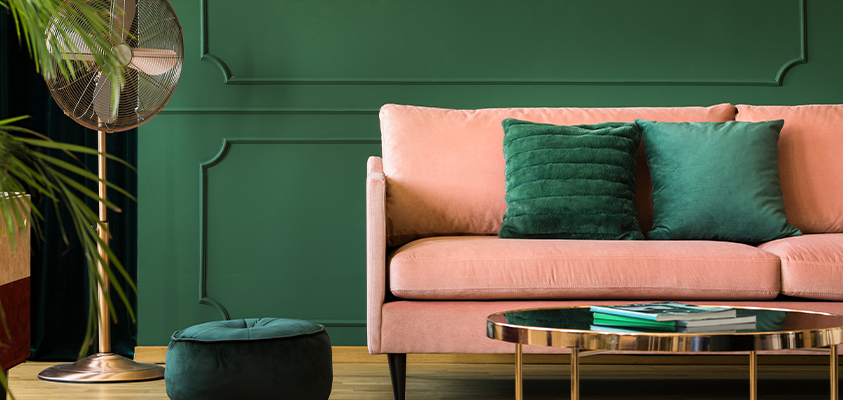 This pink sofa uses deep green throw pillows and a matching ottoman, which perfectly match the green accent wall in the background. 