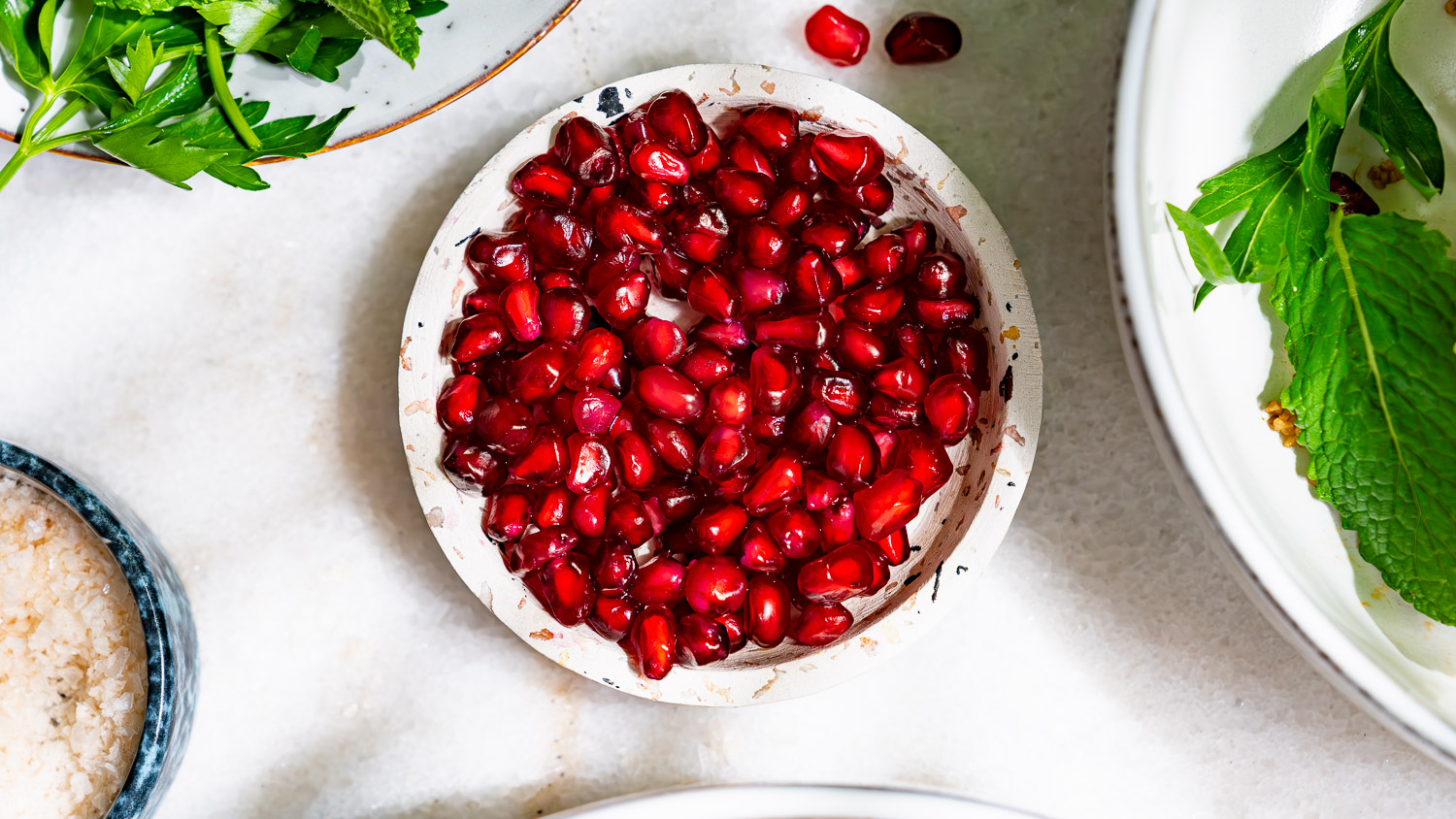 Pomegranate seeds on a small speckled plate on a white marble table.