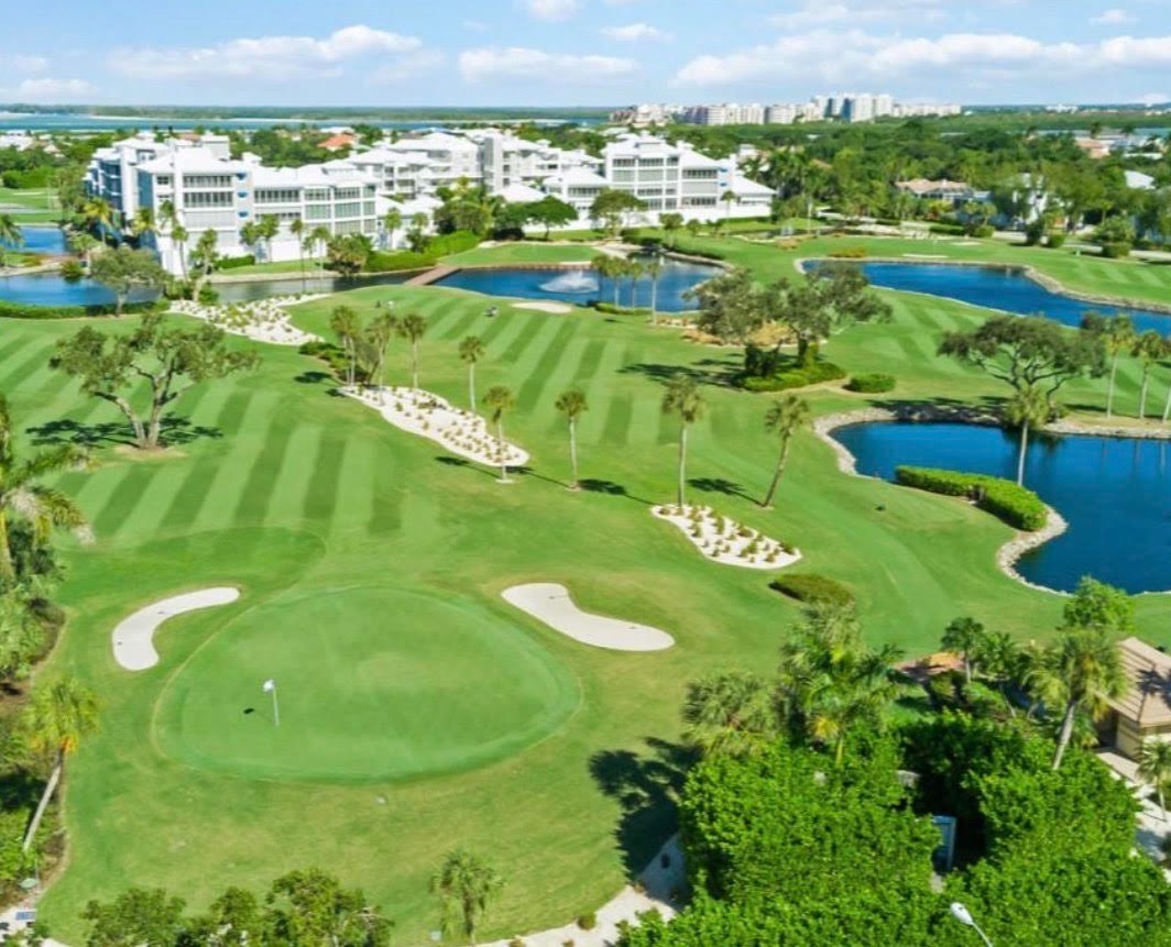 The image depicts a luxury golf course home interior featuring a gourmet kitchen with high-end appliances and custom cabinetry, seamlessly transitioning into a great room with soaring ceilings and expansive views of the golf course. This elegant living space is designed for both entertaining and comfort, showcasing the beauty of coastal living in Marco Island.