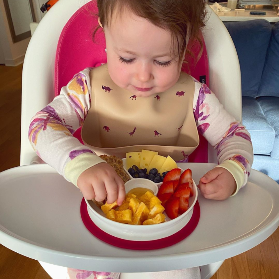 Toddler eating fruit from pink high chair seat pad of the Moon.