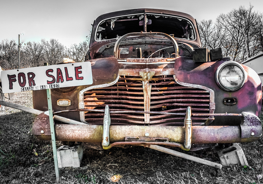 A junk car with a "For Sale" sign on it