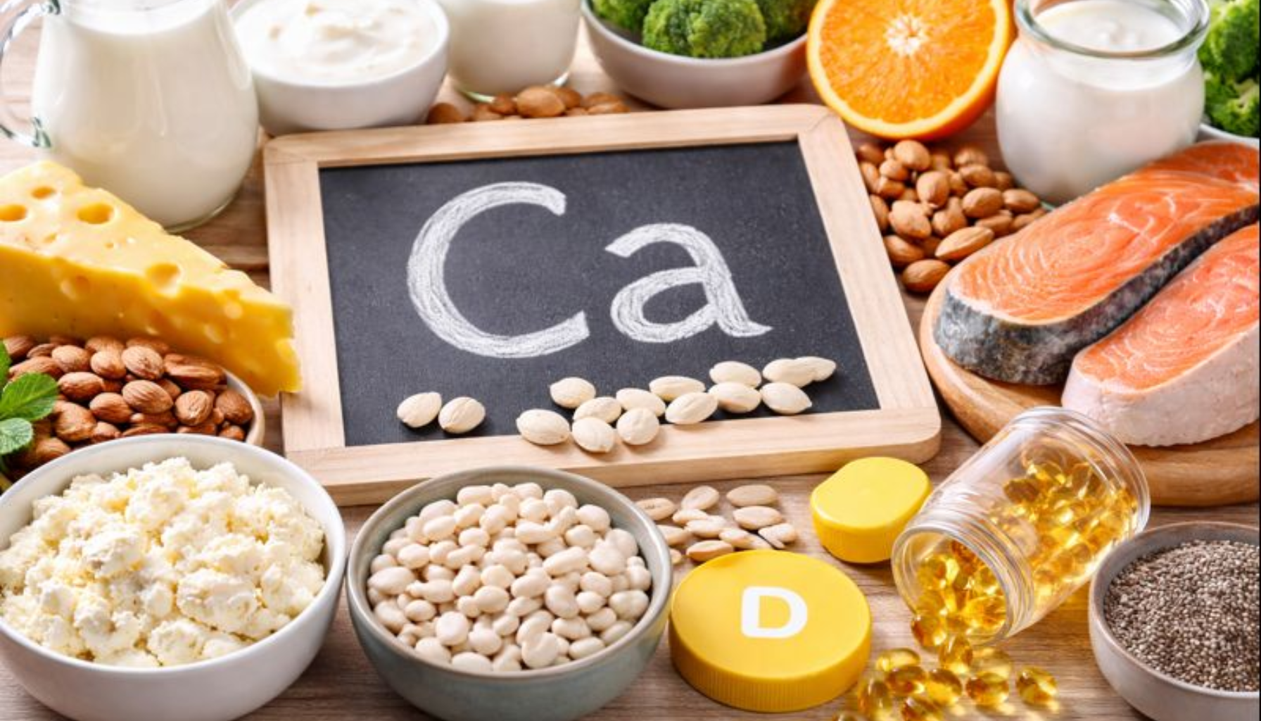 Matvarer rike på kalsium og vitamin D, inkludert laks, melk, ost, mandler og kosttilskudd, på treflate.