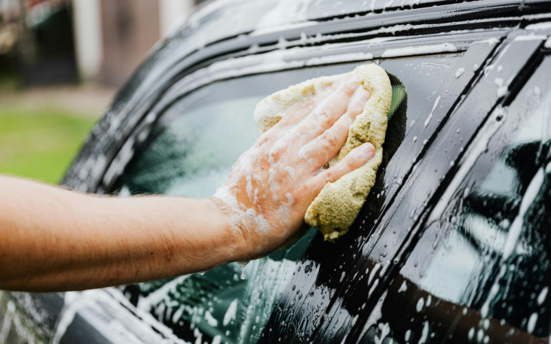 Hand washing a car window with soapy water and microfiber cloth during a car wash