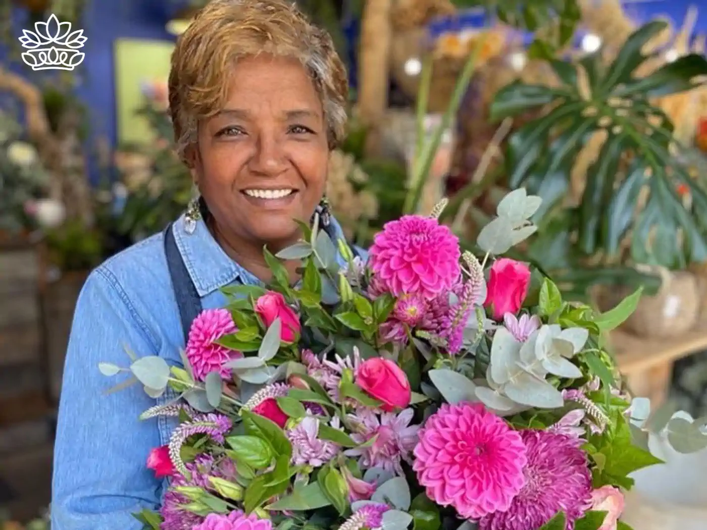 A joyful middle-aged sa florist, dressed in a blue denim shirt, holds a stunning bouquet of pink roses and dahlias, representing the vibrant life and special occasions catered by professional florists. The background showcases a well-stocked flower shop. Fabulous Flowers and Gifts.