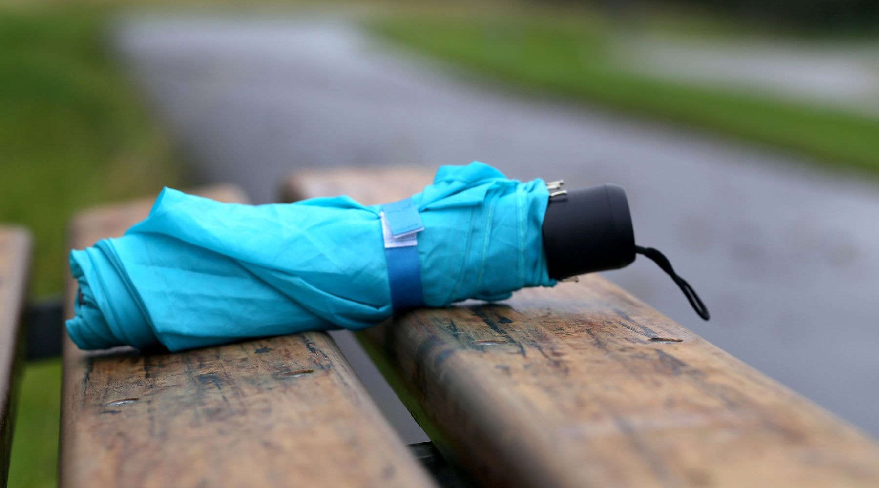 Blue umbrella folded and resting on a rainy day wooden bench.
