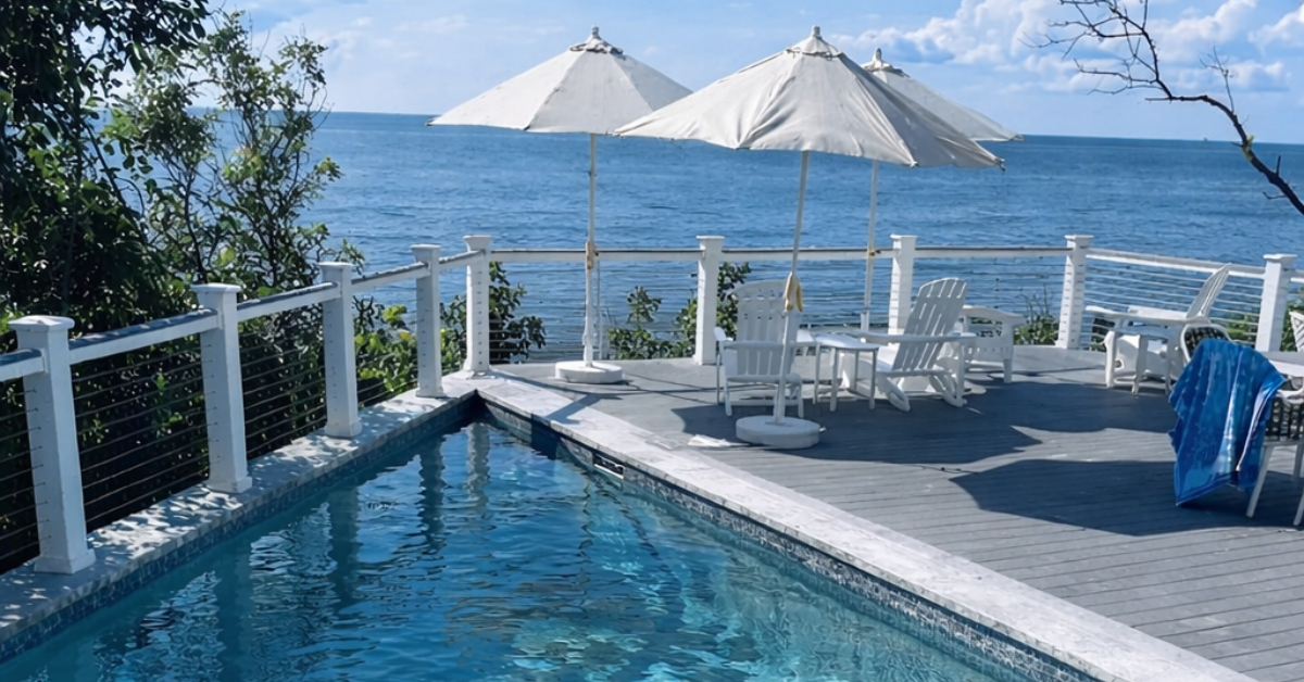 Private bayfront swimming pool with deck seating and umbrellas overlooking the Delaware Bay, offering waterfront relaxation at a Cape May villa.