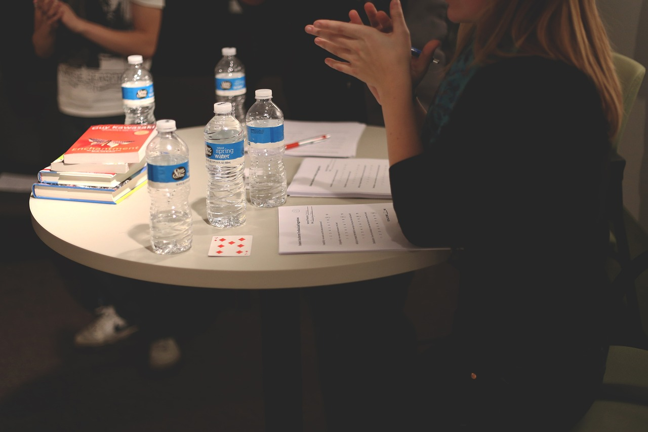 An image of a business woman sitting at a round table with several bottles of water for a meeting. 