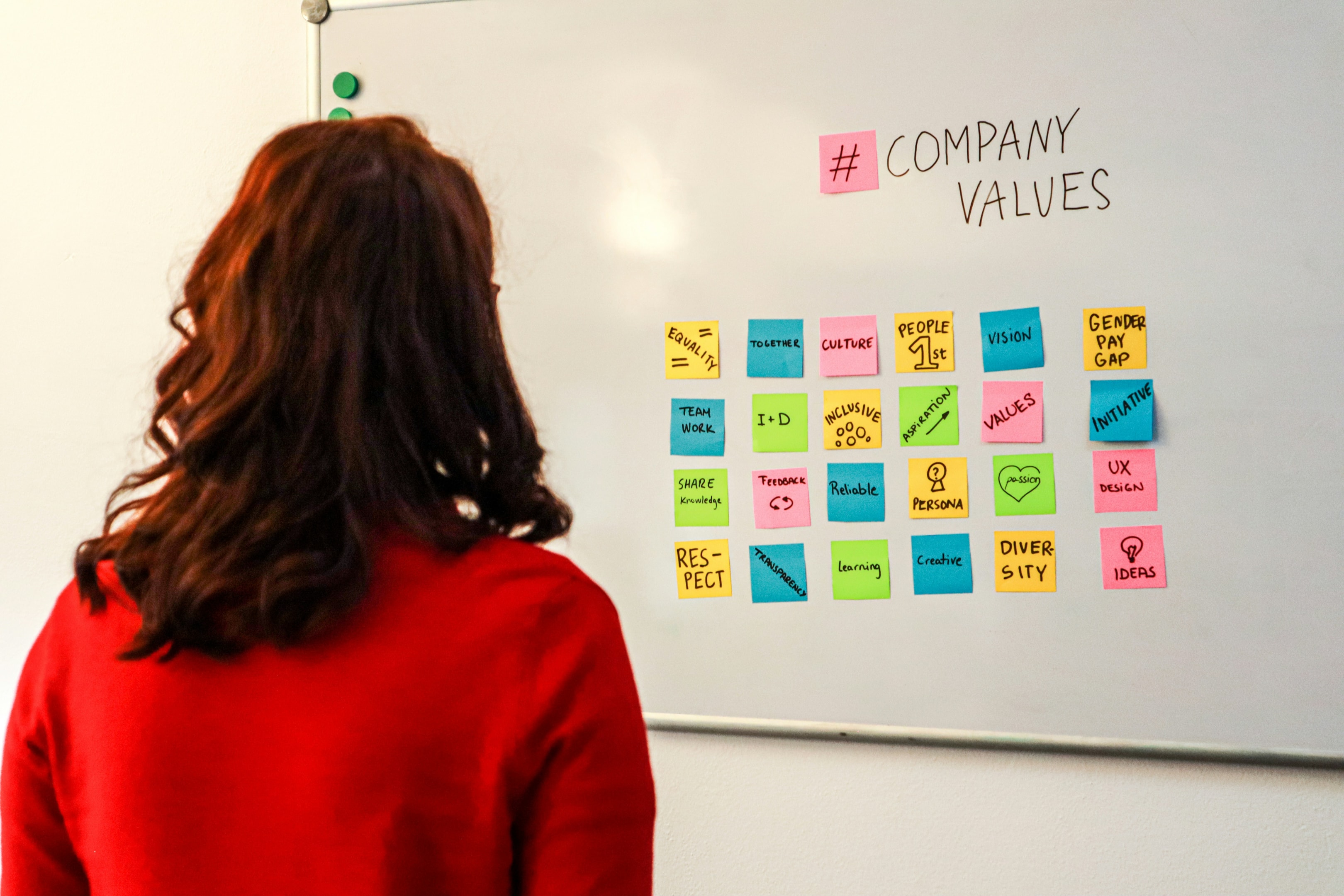 Woman in red shirt looking at whiteboard with post-it notes on it