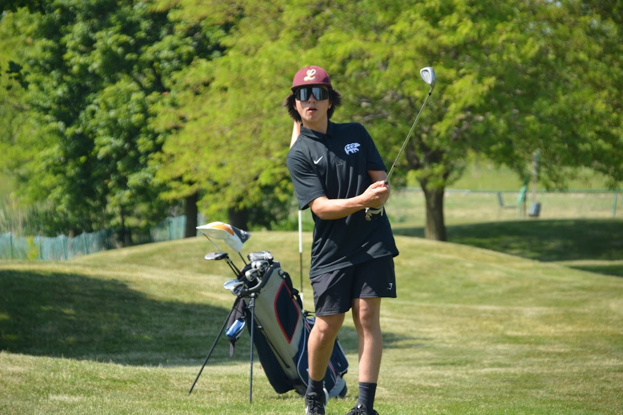 Golfer practices a short iron shot on a grassy course near a golf bag, demonstrating form and balance often trained by golf fitness trainers.