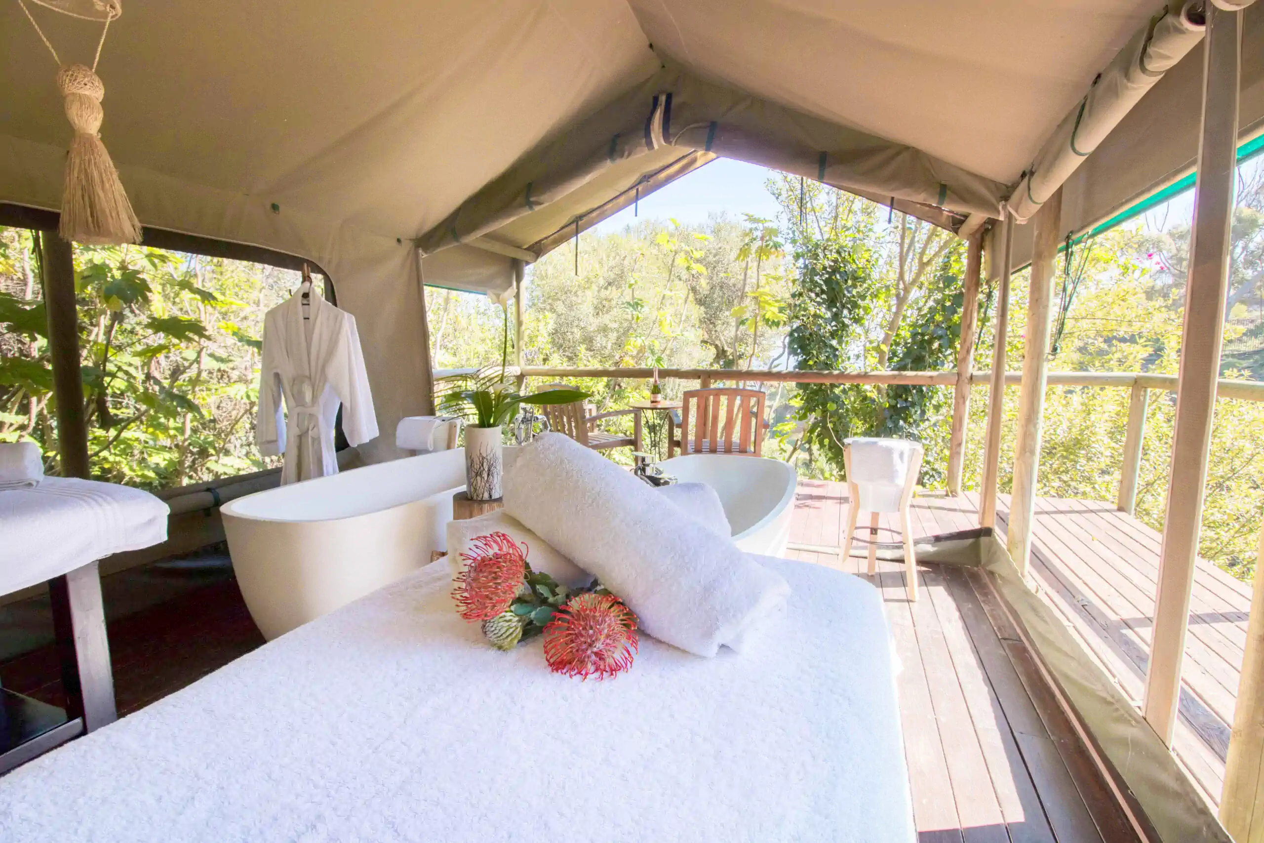 A serene spa setting with a bathtub, robe, and beautiful flowers in a canvas tent surrounded by lush greenery. Fabulous Flowers and Gifts