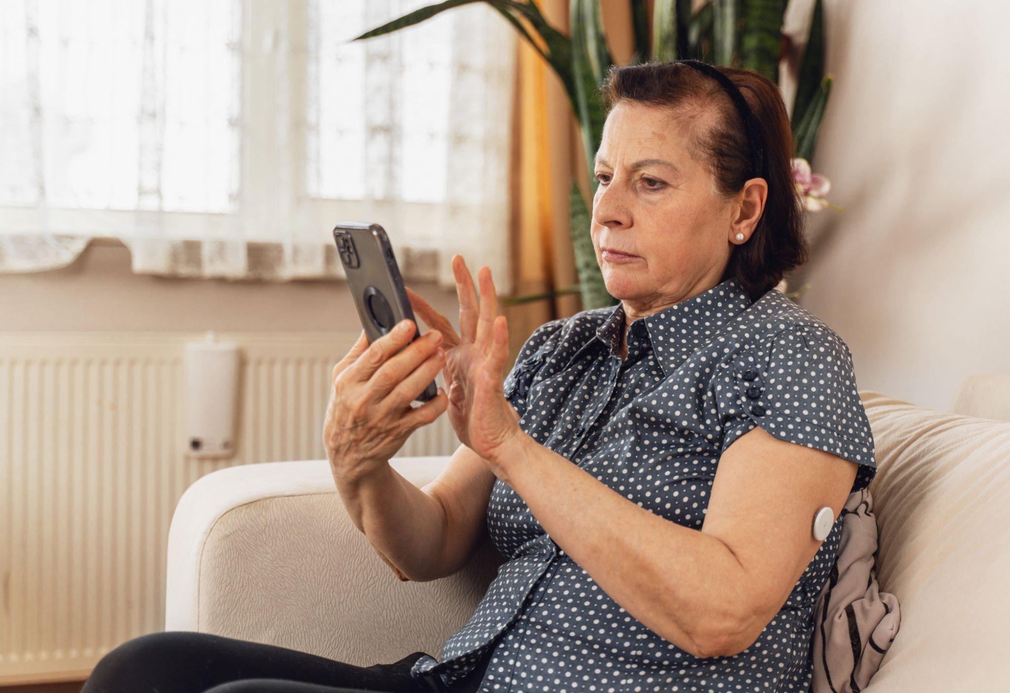 A woman wearing a CGM device, using her phone to monitor her average blood sugar levels and assess her risk of developing type 2 diabetes.