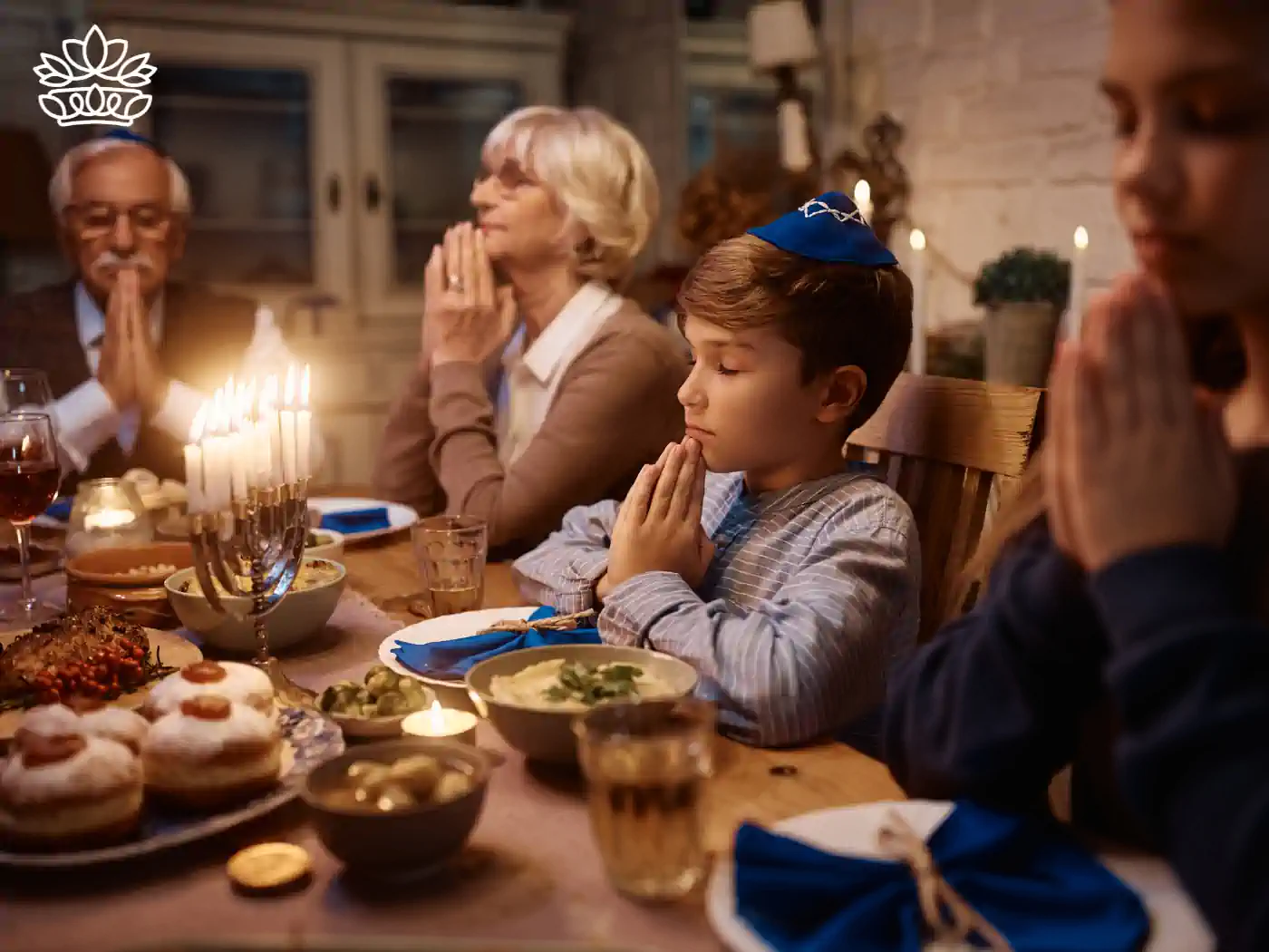 A family praying together at a Hanukkah dinner table, with a menorah and traditional dishes. Fabulous Flowers and Gifts - Hanukkah Collection.