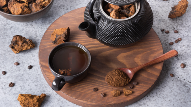 Eine Tasse Chaga-Tee, umgeben von getrockneten Stückchen des Chaga-Pilzes, auch bekannt als Inonotus obliquus. Dieser Vitalpilz wird häufig in der Volksmedizin verwendet und bietet zahlreiche Vorteile für die Gesundheit.