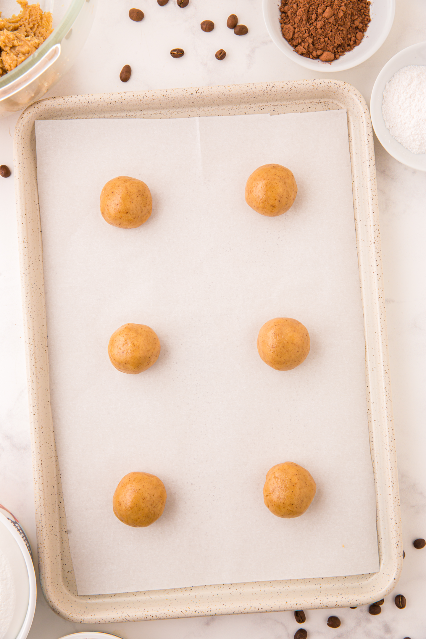 six tiramisu cookie dough balls on parchment paper lined baking sheet