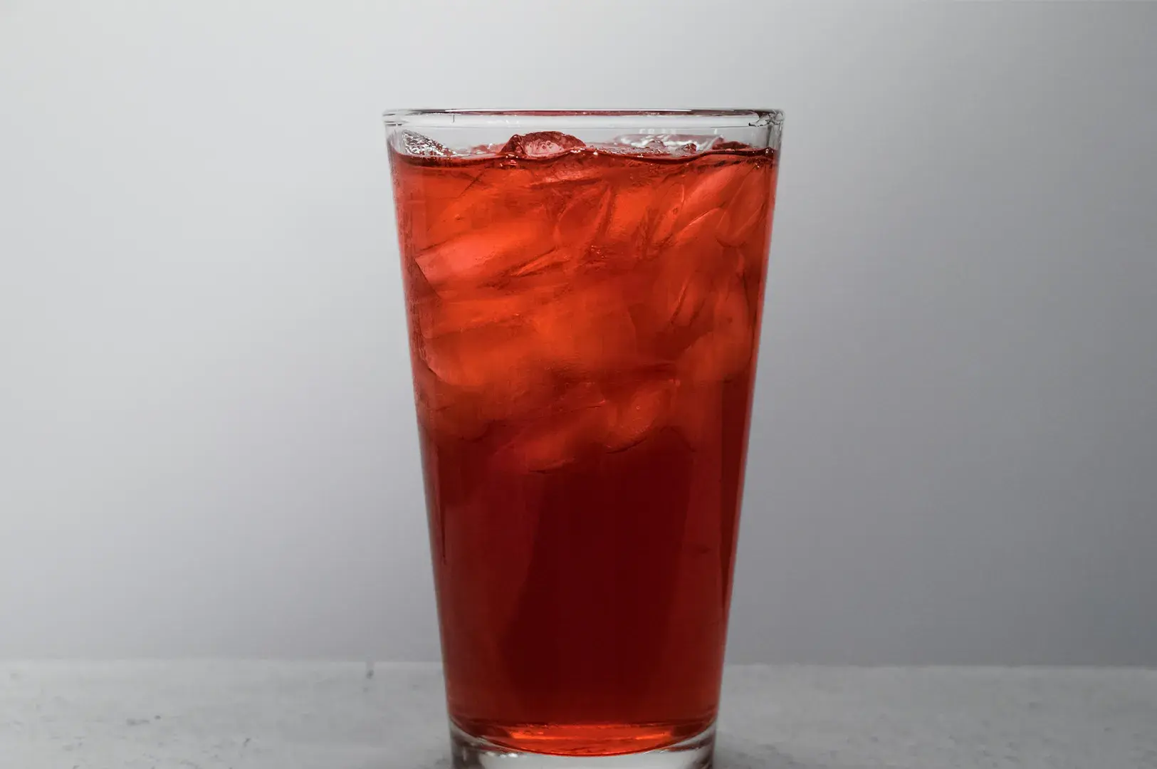 Tall glass of vibrant red iced drink packed with ice cubes.