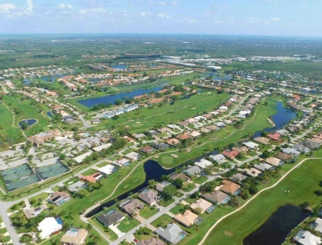 The image shows the Spanish Wells clubhouse and dining facilities, set against the backdrop of a perfectly manicured golf course in Bonita Springs, FL. The inviting architecture reflects a laid-back Florida lifestyle, complemented by the serene lake views and outdoor entertaining spaces.