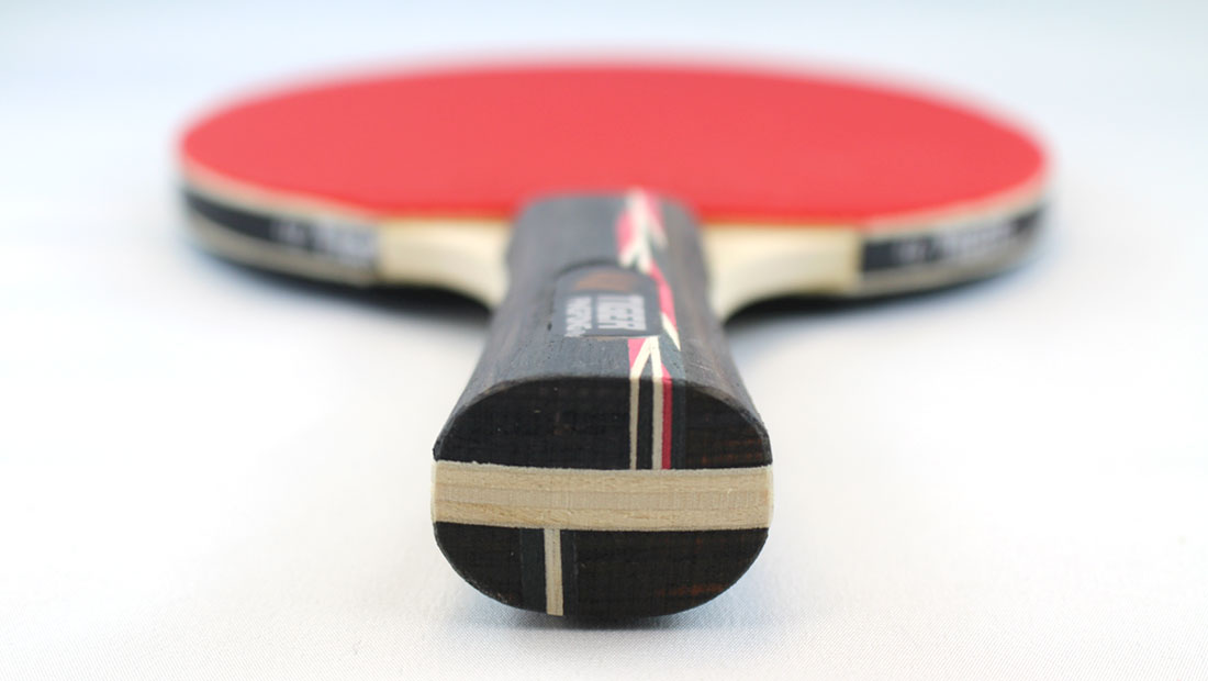 A single red ping pong paddle on a white table.