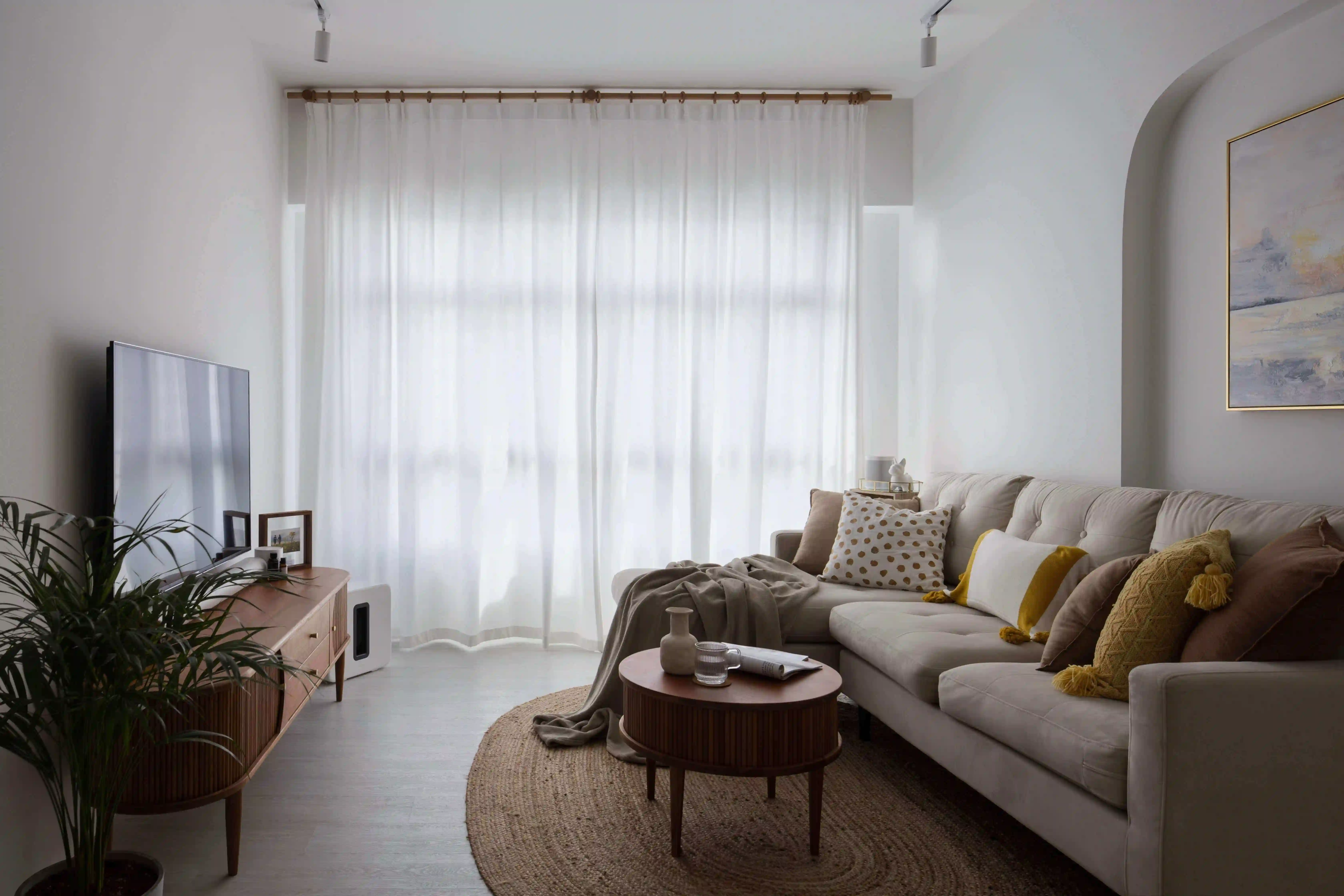 Small sitting room design with sheer curtains, slim sofa and round coffee table in a KL condo living room.